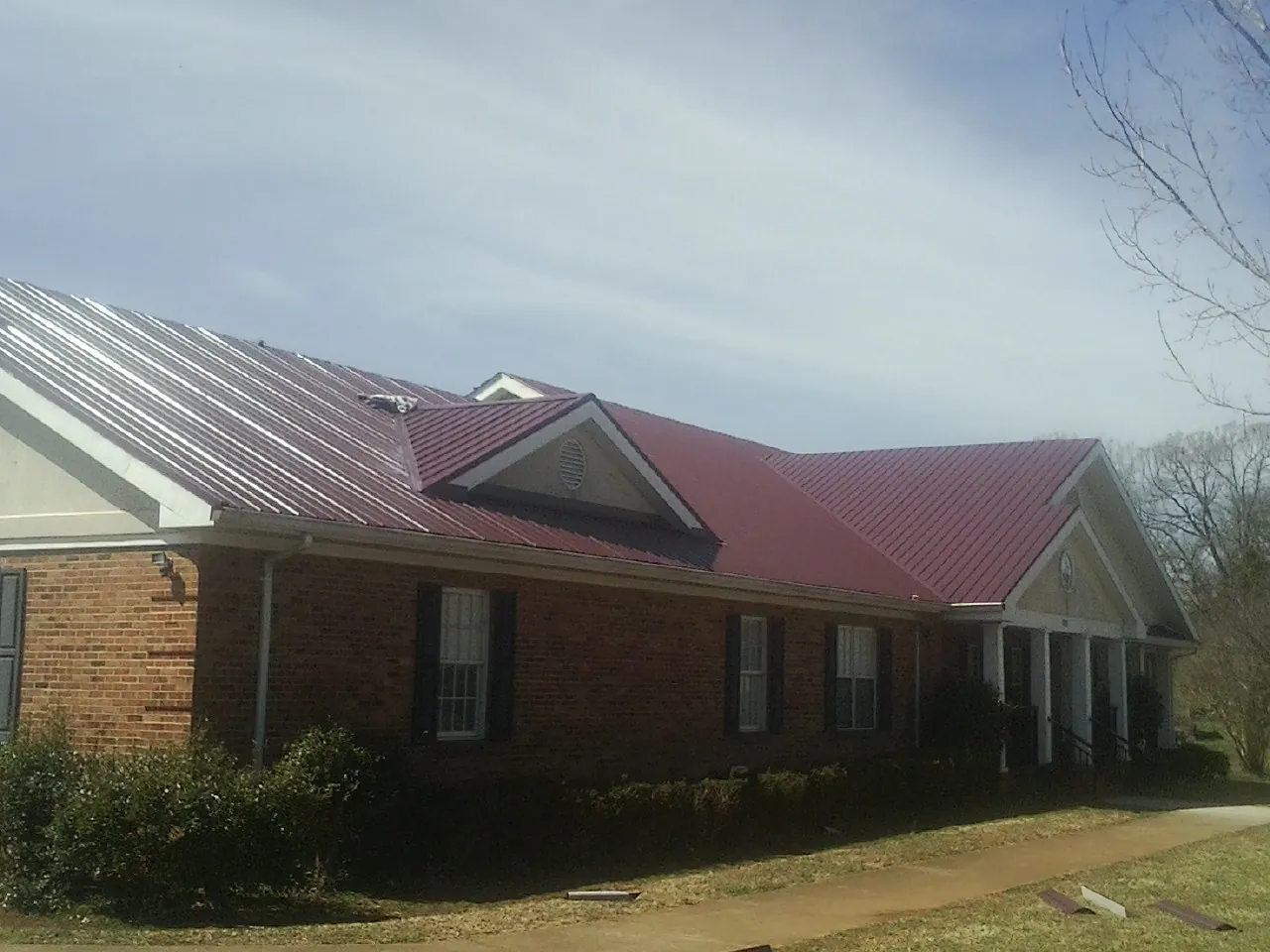 Red metal roof with gabled entries on a long brick building, from a Hail Damage Roof Repair job in Matthews
